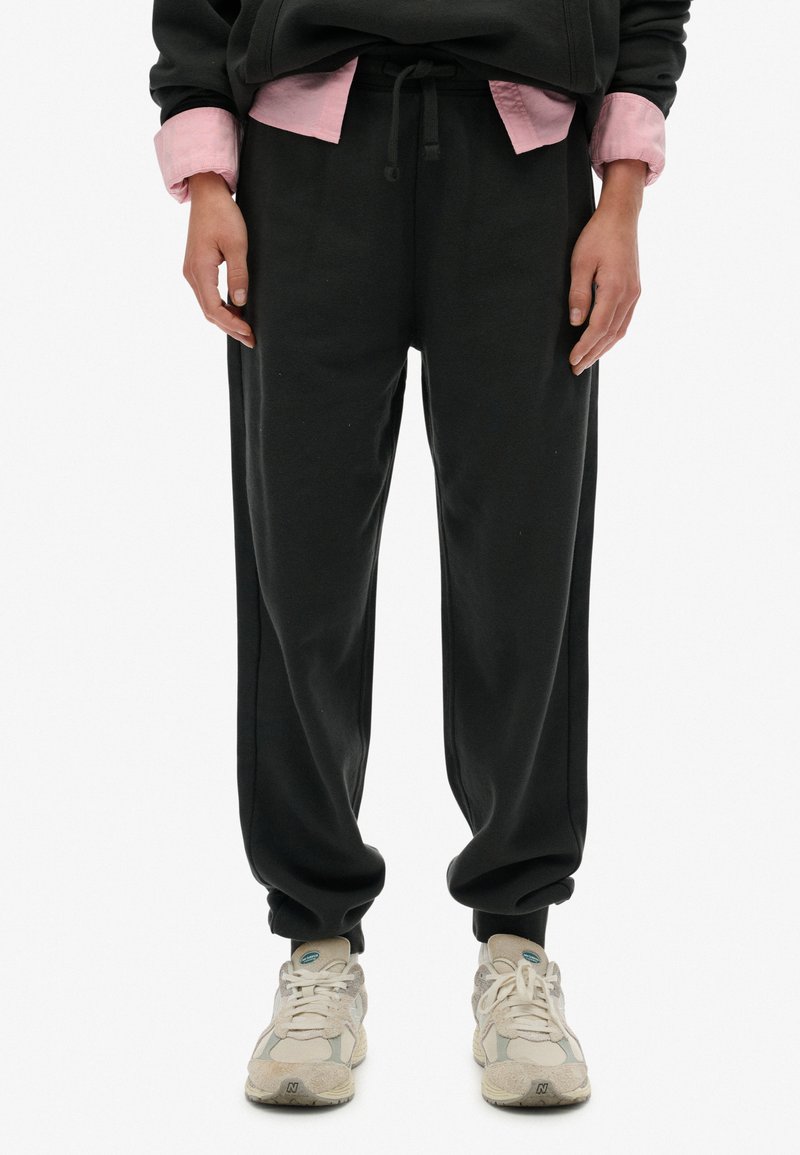 Sorte sweatpants med snøre i taljen, tapered cuffs og sidesømmer, parret med lyse sneakers. Tekstureret stof, afslappet pasform.