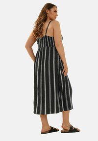 Svart och vit randig maxiklänning med en åtsittande överdel, justerbara axelband och en utsvängd kjol. Kompletterad med platta svarta sandaler.