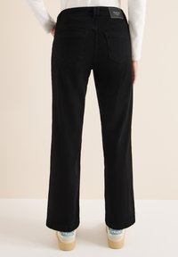 Vaqueros negros de pierna ancha con una textura suave, que cuentan con dos bolsillos traseros y una cintura con marca. Combinados con zapatillas blancas con detalles en azul.