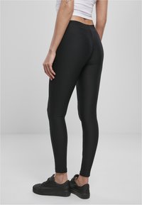 Leggings noirs côtelés avec une taille élastique, design ajusté et accents de panneau latéral ; associés à des sneakers noirs.