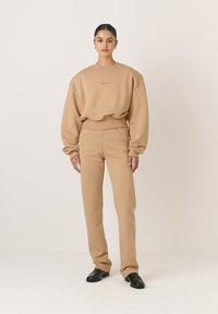 Barna, laza fazonú pulóver, bordázott alsó résszel, ami hozzáillő, szűkített nadrággal van párosítva. Mindkét darab puha tapintású és minimális díszítéssel rendelkezik.