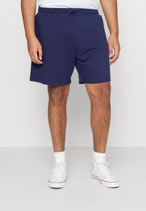 Shorts en coton bleu marine avec une taille élastique dotée d'un cordon de serrage, des poches latérales et une coupe décontractée. Portés avec des baskets blanches.