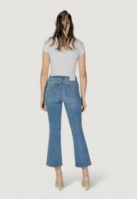 Jeans de mezclilla azul de corte acampanado con una cintura de altura media, diseño de cinco bolsillos y costuras visibles. Combinados con una blusa blanca ajustada y zapatos en tonos neutros.