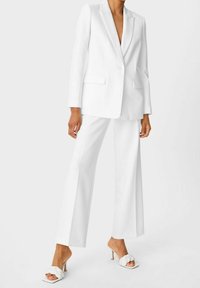 Biała skrojona marynarka i pasujące szerokie spodnie, wykonane z gładkiego materiału. Posiada czyste linie i zapięcie na jeden guzik.