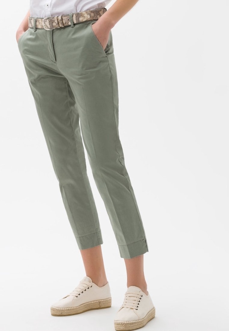Ljusgröna bomullsbyxor i cropped-modell med framfickor och rullad fåll, matchade med ett mönstrat bälte och vita espadrilles-sneakers.