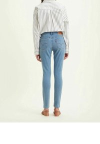 Jeans ajustados de color azul con una cintura de media altura, que presentan un parche de cuero en la parte trasera y costuras sutiles en los bolsillos traseros, combinados con una camisa a rayas.