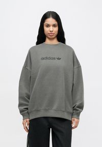 Γκρι φαρδιά φούτερ με στρογγυλή λαιμόκοψη που διαθέτει τονόμορφο λογότυπο «adidas». Κατασκευασμένο από απαλό ύφασμα, έχει χαμηλωμένους ώμους και ριμπ μανσέτες.