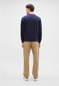 Granatowy sweter z ściągaczami na mankietach, zestawiony z jasnobrązowymi spodniami z sztruksu. Model w białych trampkach, widok z tyłu.