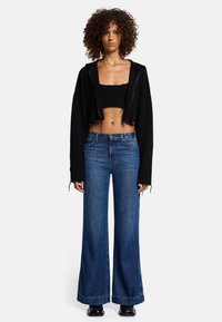 Gekürzter schwarzer Hoodie über einem enganliegenden schwarzen Top, kombiniert mit weit geschnittenen blauen Jeans. Verfügt über fransige Kanten und eine entspannte Silhouette.