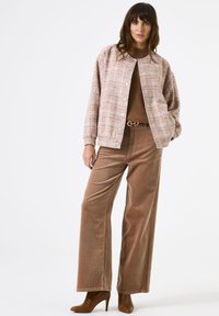 Roze tweed jasje met ronde hals en knoopsluiting, gecombineerd met bruine corduroy wijde broek en bruine haklaarzen.