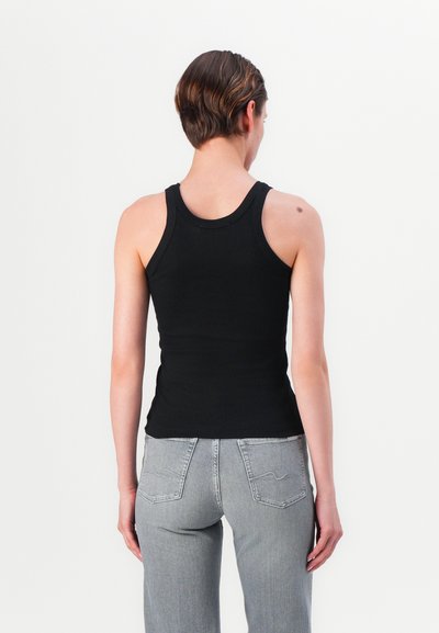 Must mustribbiga tank top, mis on sobiva disainiga ja ringikujulise kaelusega, koos heledate hallide sirgete pükstega, nähtud tagant.