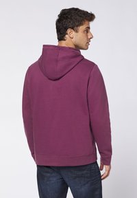 Purple hooded sweatshirt, cotton blend, fitted design, ribbed cuffs and hem, smooth texture, displayed from the back against a light background.