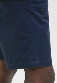 Marineblå bomuldsshorts med en glat overflade, præsenteret med en lige snit og omhyggeligt færdiggjorte kanter. Nærbillede af stoffet.