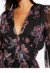 Sort kjole med blomstermønster, der har en dyb V-hals, lange gennemsigtige ærmer og knapdetaljer i taljen. Glat, let stof.