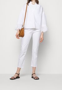 Bílý bavlněný top s objemnými volánkovými rukávy, zkombinovaný s bílými přiléhavými zkrácenými kalhotami a černými sandály na podpatku s pásky. Hnědá křížová taška.