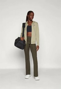 Outfit sportivo composto da una felpa leggera olive con zip, reggiseno sportivo nero, pantaloni aderenti verde oliva e scarpe bianche. Borsa da palestra nera a tracolla.