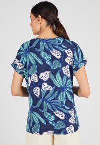 Blusa a maniche corte in blu navy con un vivace motivo di foglie tropicali in verde e crema. Tessuto morbido con una vestibilità rilassata e maniche arrotolate.