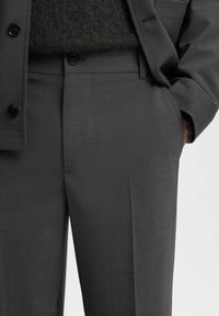 Graue maßgeschneiderte Hose mit glatter Textur, flachem Vorderteil, seitlichen Taschen und einem subtilen Schimmer, kombiniert mit einem dunklen, flauschigen Pullover.