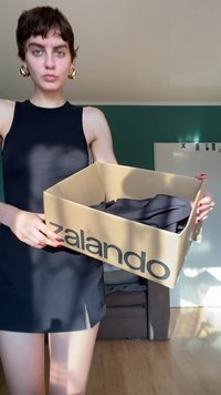 Juodas „Zalando“ dežė, laikoma atvira, joje yra tamsi medžiaga. Dežė turi didelį logotipą ir yra pagaminta iš kartono. Fone matoma šviesių medžio grindų.