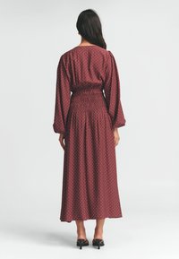 Bordo midi šaty s bílými puntíky, smocked pasem, širokými rukávy a splývavým siluetou. Hladká textura látky.