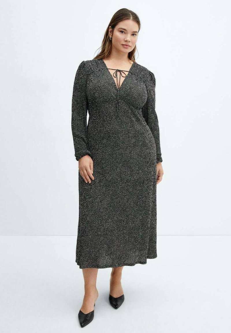 Abito lungo a macchie nere e argento con scollatura a V profonda e chiusura con nastro, caratterizzato da maniche lunghe e una gonna fluida, abbinato a scarpe nere.