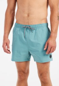 Svetlomodré plavky s elastickým pásom a čierno-bielou šnúrkou, so malým kruhovým logom na dolnej časti nohy.