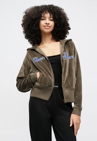 Corta e verde-oliva, camisola com capuz e fecho zip em veludo macio com texto bordado. Apresenta um capuz e bolsos laterais, com um corte justo e punhos canelados.