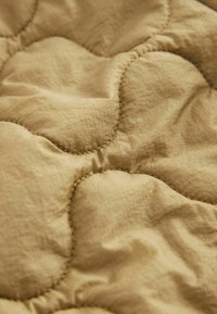Gros plan d’un tissu matelassé beige avec des coutures courbes et une texture douce et rembourrée.