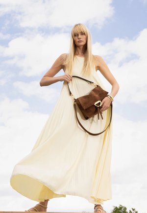 Beige Wildleder-Handtasche mit braunem Lederriemen und goldfarbener Schnalle, kombiniert mit einem fließenden, plissierten hellgelben Kleid.