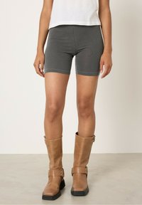 Sive raztegljive kolesarske hlace v kombinaciji s srednje dolgimi rjavimi usnjenimi škornji z zaponkami in kvadratnim prstom.