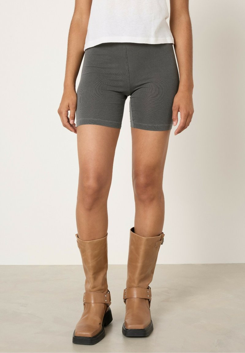 Sive raztegljive kolesarske hlace v kombinaciji s srednje dolgimi rjavimi usnjenimi škornji z zaponkami in kvadratnim prstom.