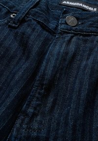 Jeans in denim con una tonalità blu scuro e sottili righe verticali, bottone in metallo in vita e dettagli di tessuto strutturato vicino alle cuciture.