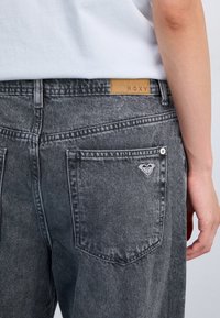 Grå denimjeans med en lærmerke fra Roxy i midjen, brodert hjerte-logo på baklommen og rett ben.