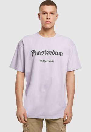 Light purple cotton t-shirt featuring black text reading "Amsterdam" and "Netherlands" in a bold, Gothic font. Relaxed fit with short sleeves.