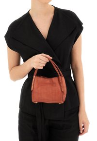 Borsa a tracolla in pelle marrone con borchie dorate ai lati, forma rettangolare e manici corti. Indossata da una persona con una maglietta nera.