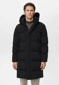 Abrigo acolchado negro con capucha, que presenta un cierre de cremallera, dos bolsillos laterales y un diseño acolchado para aislamiento. Textura suave y mate.