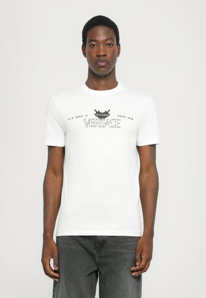 White cotton t-shirt featuring a black graphic print with text and design elements from Versace, crew neckline, short sleeves, and standard fit.