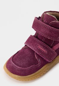 Velcro-rikschoen in diep paars suede, met een rubberen zool met gripstructuur, zachte bontvoering en contrasterende stikseldetails.