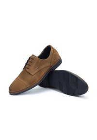 Zapatos de ante marrón con un diseño clásico, que presentan una punta redondeada, cordones en la parte frontal y una suela de goma texturizada para mayor agarre.