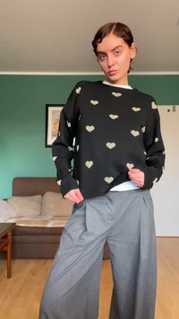 Juodas megztinis su auksinėmis širdies raštais, apvalia apykakle ir kašmyro rankogaliais, derinamas su pilkomis plačiomis kelnėmis, vidinėje erdvėje.