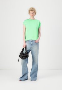 Un haut à manches courtes vert fluo associé à un jean ample bleu clair. La tenue comprend un sac noir avec des motifs floraux et des accents froncés.