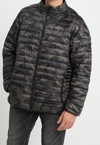 Polstret sort og grå camouflagejakke med lynlås foran, høj krave og vandret quiltet design. Glat tekstur med en almindelig pasform.