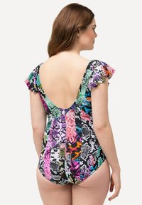 Femme aux longs cheveux bruns portant un maillot de bain à motifs colorés avec des manches à volants et un dos plongeant, de dos sur un fond blanc.