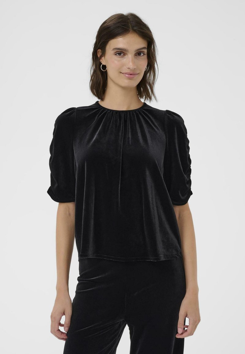 Top in velluto nero con scollatura arricciata, maniche a sbuffo corte e vestibilità facile. Texture liscia con un leggero luccichio. Senza fantasie né accessori.