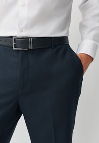 Navy textured trousers with a sleek fit, paired with a black belt featuring a rectangular silver buckle and a white button-up shirt.