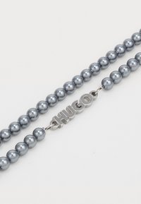 Grå pärlarmband med glansiga sfäriska stenar, med en silverfärgad metalledning som visar varumärket "HUGO."