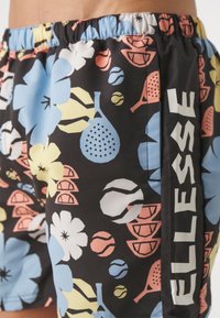 Los pantalones cortos de baño presentan un fondo negro con coloridos patrones florales y deportivos en azul, rosa y amarillo. Cintura elástica; detalle de logo en el lateral.
