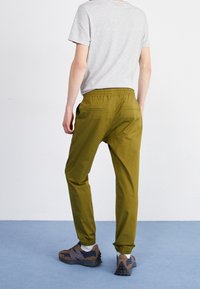 Gröna joggingsbyxor med elastisk midja, sidofickor och åtsittande muddar, tillsammans med en grå t-shirt och bruna/grå mönstrade sneakers.