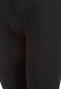 Schwarze Leggings aus dehnbarem Stoff. Glatte Textur mit einem körpernahen Design und kontrastierenden Nähten entlang der Nähte. Keine sichtbaren Muster.