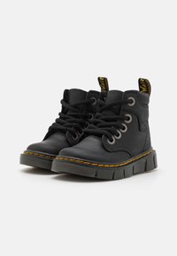 Botas de tobillo de cuero negro con puntera redonda, superficie texturizada, seis ojales metálicos y cordones negros. Presentan costuras amarillas y una lengüeta.